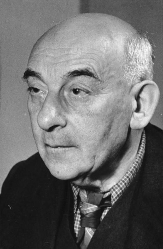 Black and white portrait of Victor Klemperer, a bald man who appears white looking off to the left side of the frame. He is wearing a tie and a dark sweater of some kind.